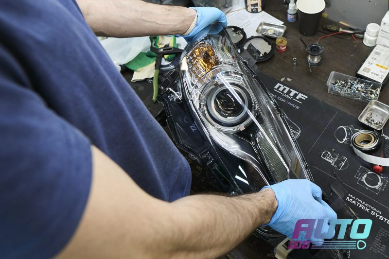 Мастер вжимает новое стекло в герметик фары Mazda 6 GJ